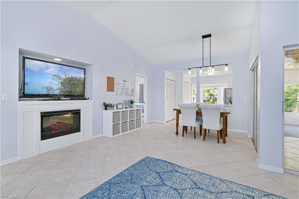 Dining space featuring a healthy amount of sunlight, light tile patterned floors, a glass covered fireplace, and lofted ceiling