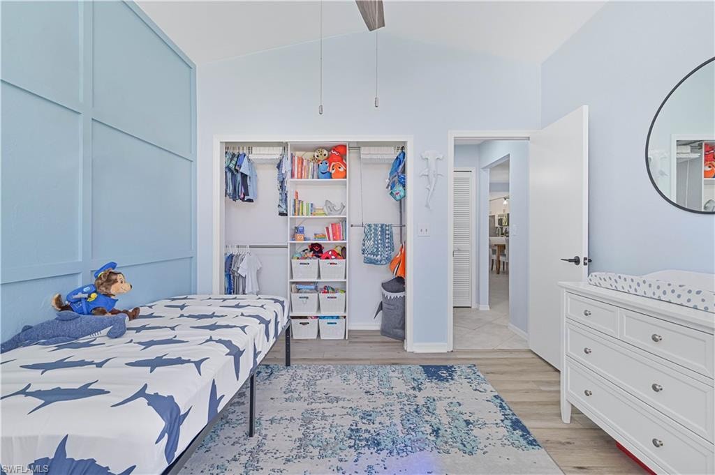 Bedroom with a closet, baseboards, lofted ceiling, and light wood-type flooring