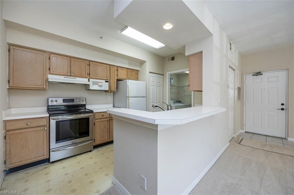 Kitchen with white appliances, under cabinet range hood, washing machine and dryer, light countertops, and recessed lighting