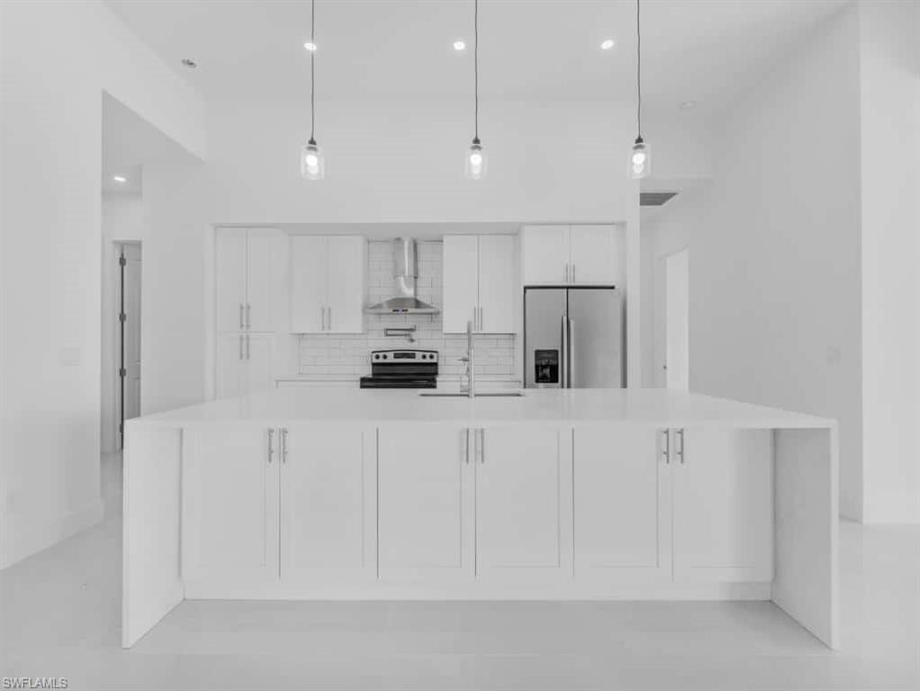 Kitchen with appliances with stainless steel finishes, wall chimney exhaust hood, light countertops, white cabinetry, and decorative backsplash