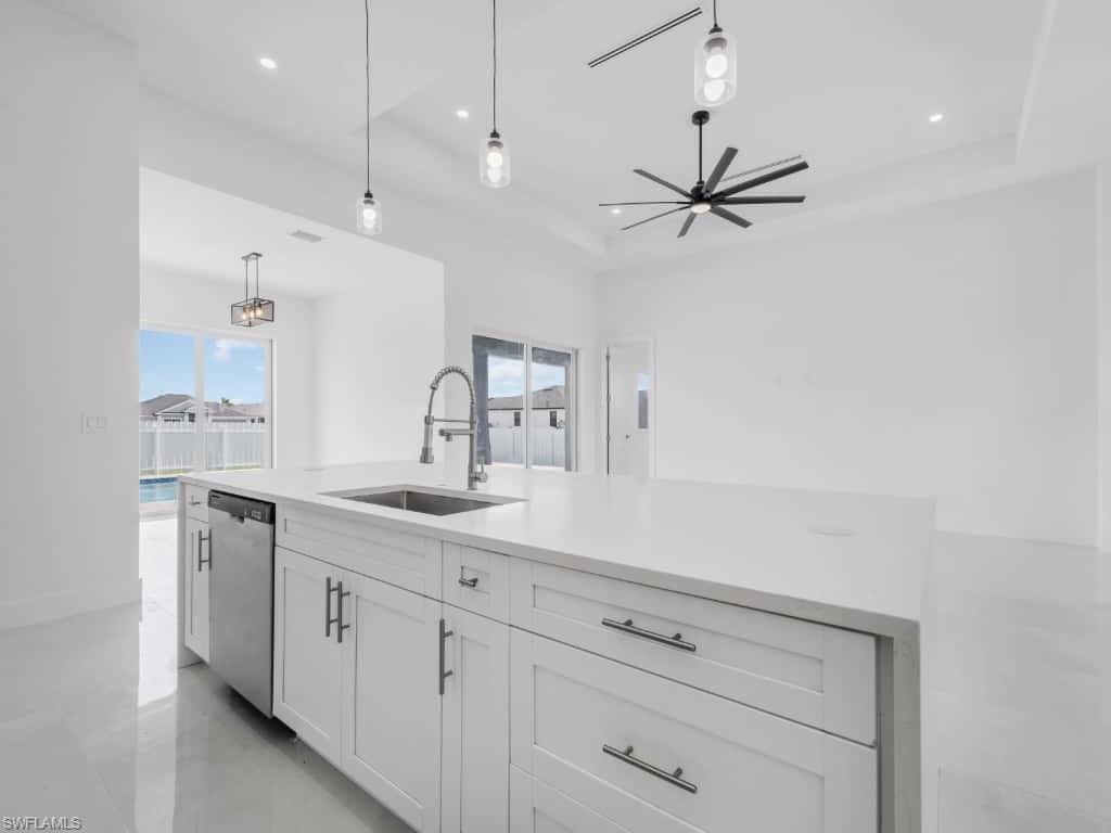 Kitchen featuring stainless steel dishwasher, light countertops, a tray ceiling, a ceiling fan, and white cabinets
