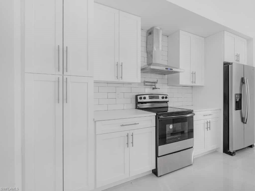 Kitchen with stainless steel fridge with ice dispenser, tasteful backsplash, wall chimney range hood, light countertops, and white cabinetry