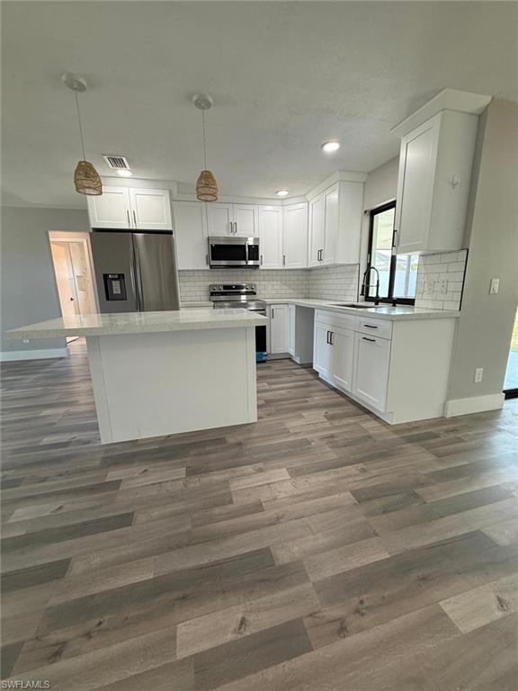 Kitchen featuring wood finished floors, a sink, white cabinets, backsplash, and appliances with stainless steel finishes