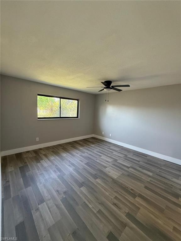 Unfurnished room with dark wood-style flooring, baseboards, and a ceiling fan