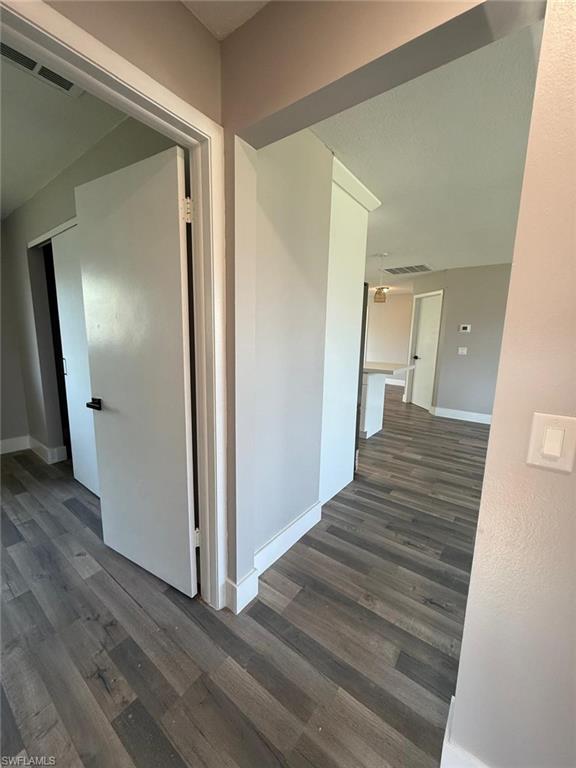 Hallway featuring baseboards, dark wood-style flooring, and visible vents