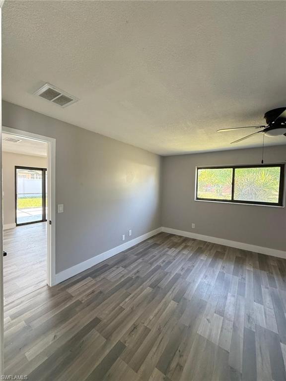 Spare room with wood finished floors, a textured ceiling, visible vents, a ceiling fan, and baseboards