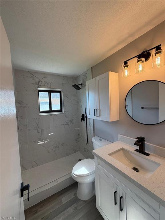 Full bath featuring a textured ceiling, toilet, vanity, wood finished floors, and a marble finish shower