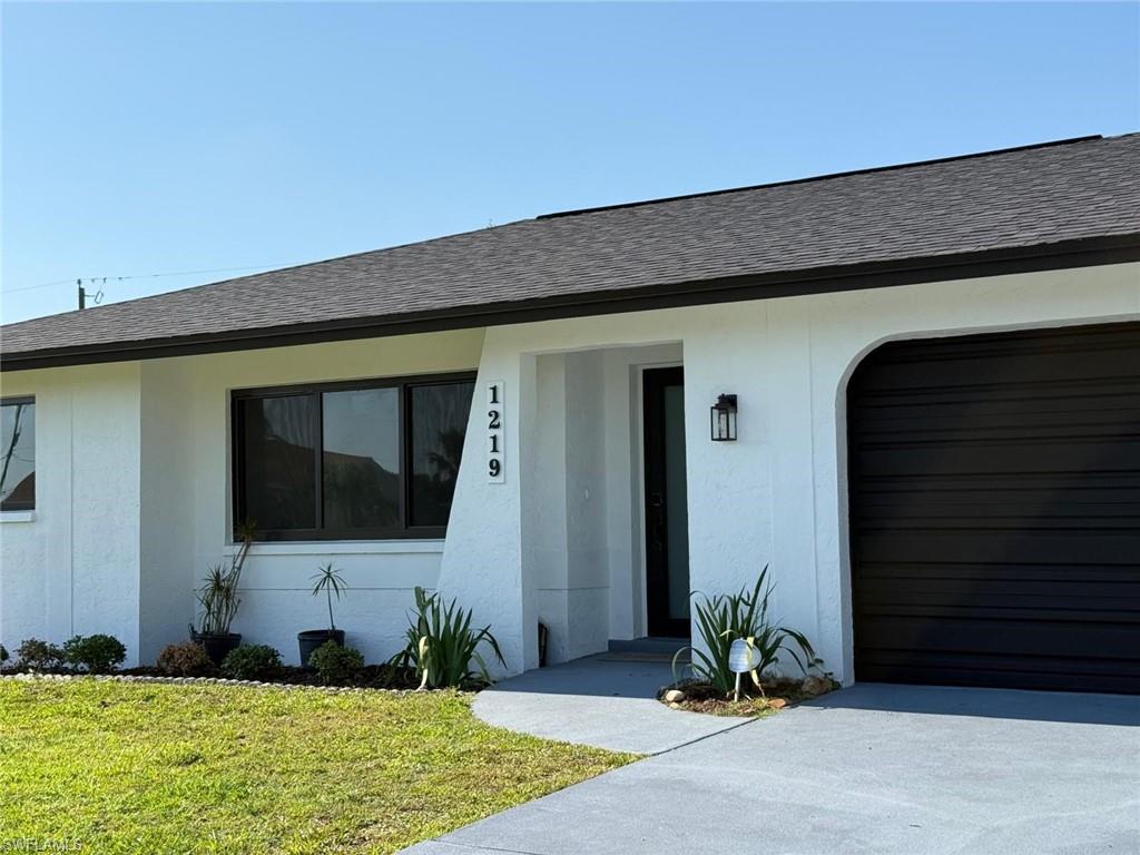 View of front facade featuring a shingled roof, stucco siding, an attached garage, and a front lawn