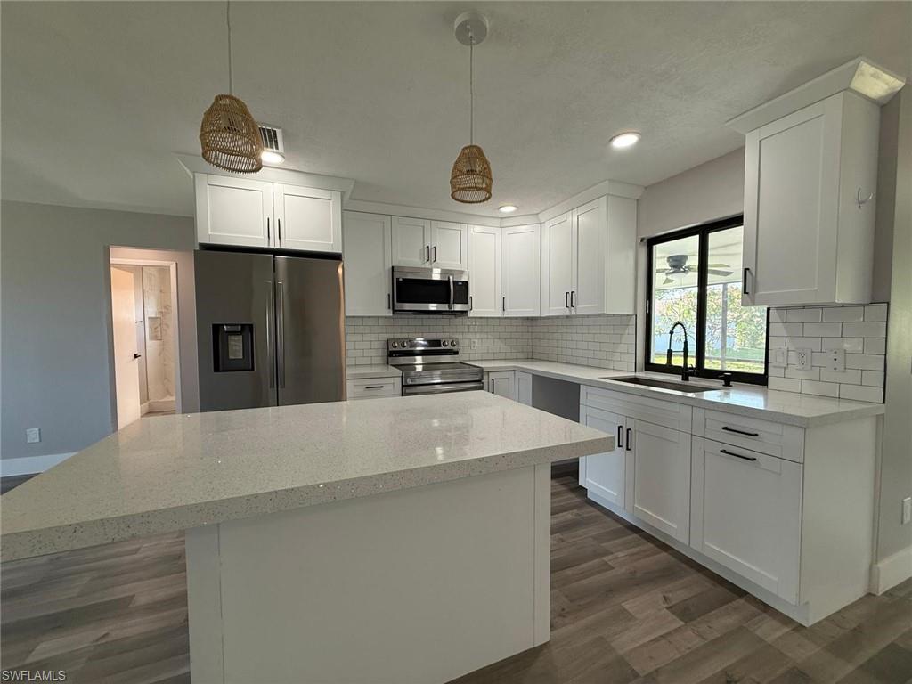 Kitchen featuring dark wood finished floors, a sink, a kitchen island, backsplash, and appliances with stainless steel finishes
