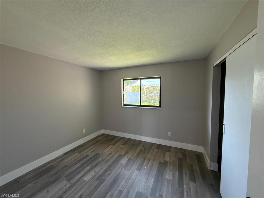 Unfurnished bedroom featuring dark wood-style flooring, a textured ceiling, baseboards, and a closet