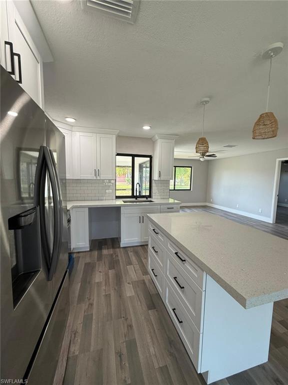 Kitchen featuring stainless steel fridge, visible vents, dark wood-style floors, and white cabinets