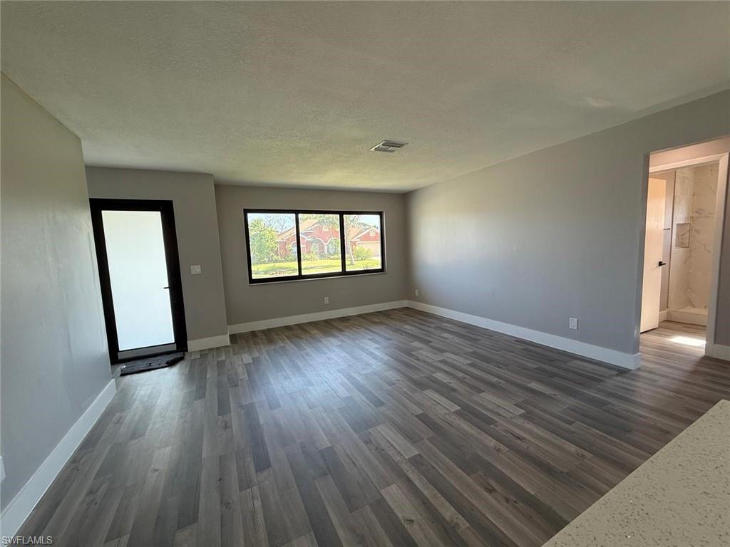 Spare room featuring a textured ceiling, baseboards, dark wood-type flooring, and visible vents