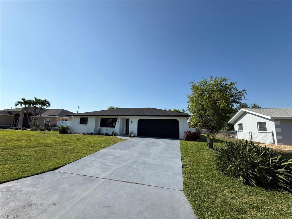 Ranch-style home with driveway, fence, a garage, stucco siding, and a front yard