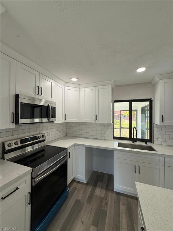 Kitchen featuring dark wood-style flooring, stainless steel appliances, white cabinets, and a sink