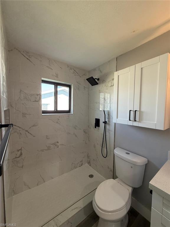 Full bath featuring toilet, tiled shower, and vanity