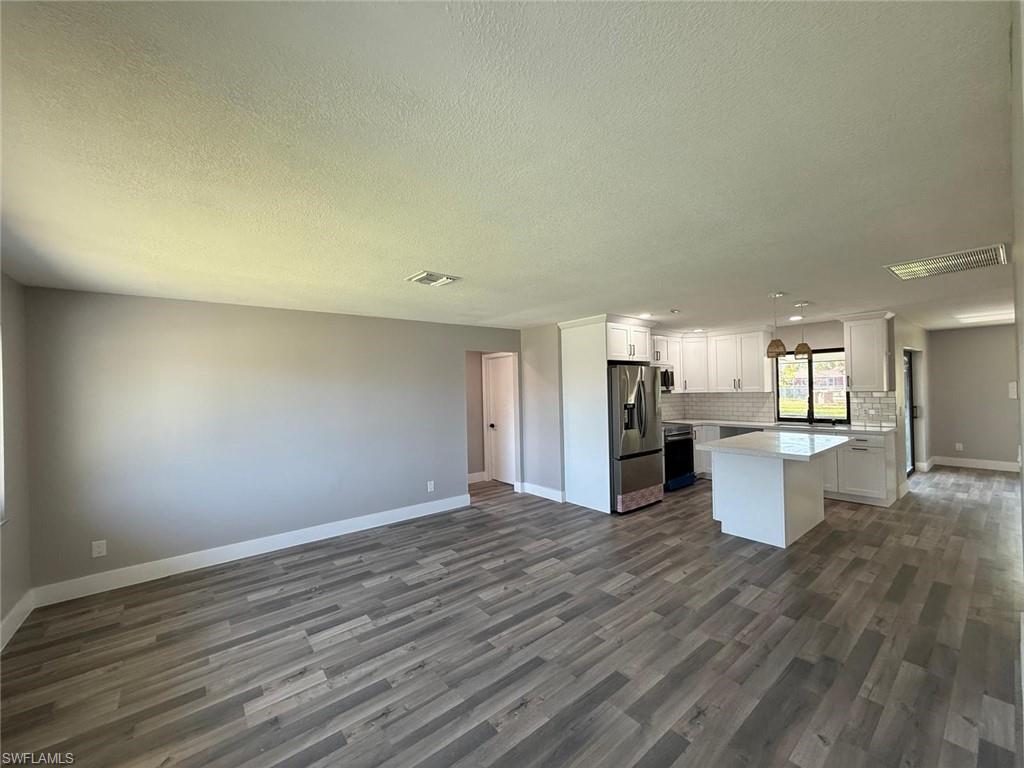 Kitchen featuring stainless steel refrigerator with ice dispenser, dark wood-type flooring, backsplash, open floor plan, and baseboards