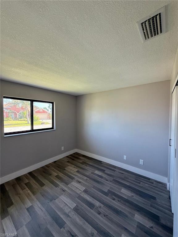 Spare room featuring baseboards, dark wood finished floors, visible vents, and a textured ceiling