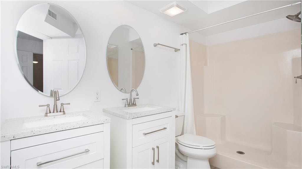 Primary bathroom with a shower stall, two vanities, and toilet