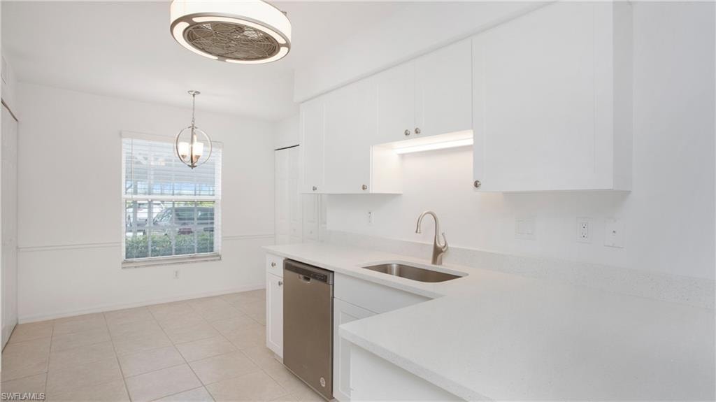 Kitchen featuring stainless steel dishwasher, a sink, light countertops, white cabinets, and pendant lighting