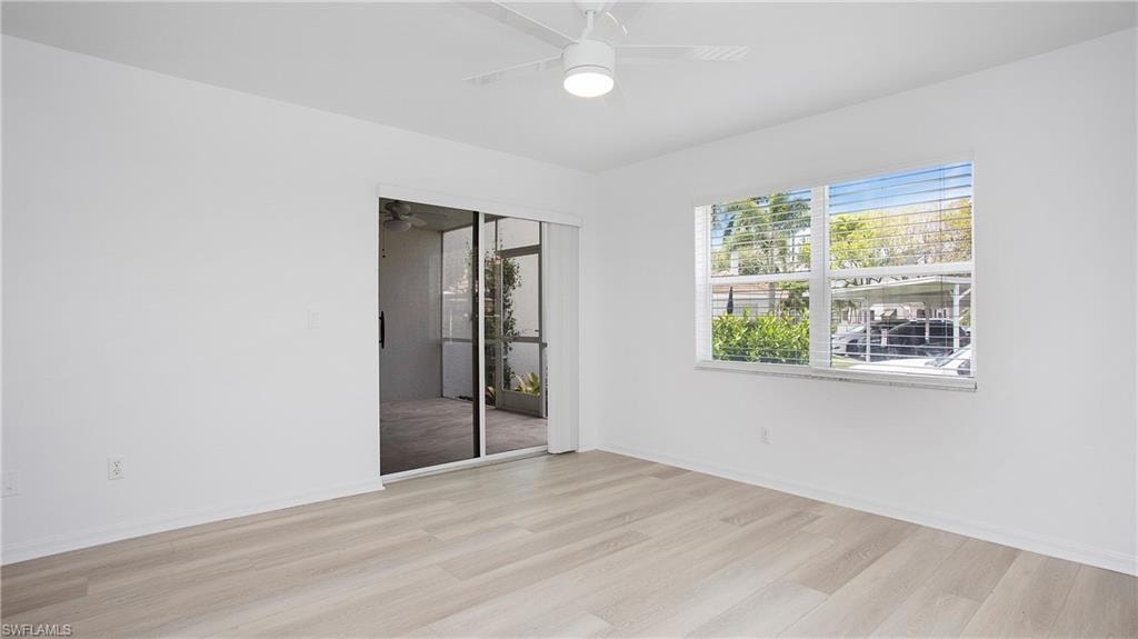 Primary bedroom featuring light wood finished floors, a ceiling fan, and baseboards. Slider opens to the lanai.