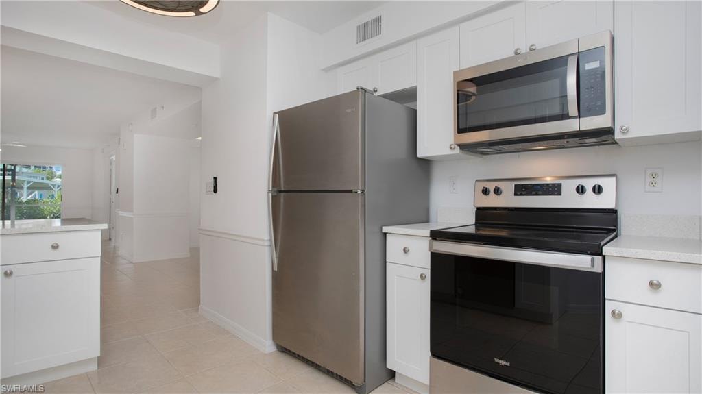 Kitchen with stainless steel appliances, light countertops, white cabinetry, and light tile patterned floors