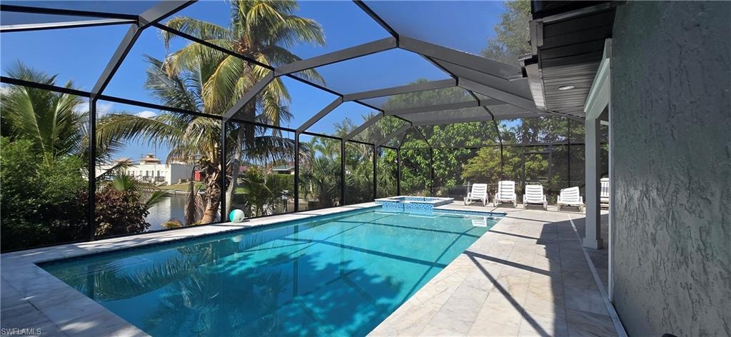 View of pool featuring a patio area, a pool with connected hot tub, a water view, and glass enclosure