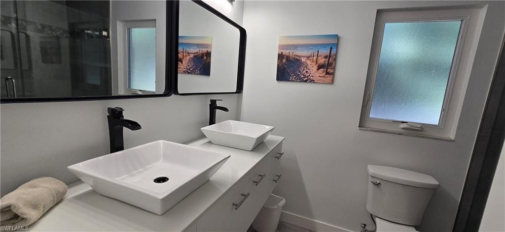 Bathroom featuring toilet, a shower with door, baseboards, and double vanity
