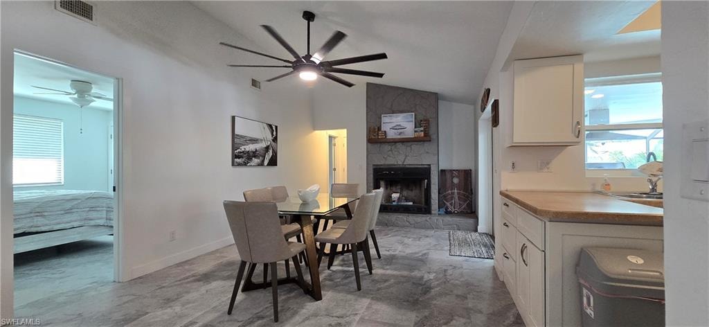 Dining space with a ceiling fan, a stone fireplace, vaulted ceiling, and baseboards