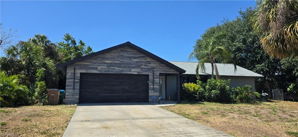 Single story home featuring driveway, a garage, and stone siding