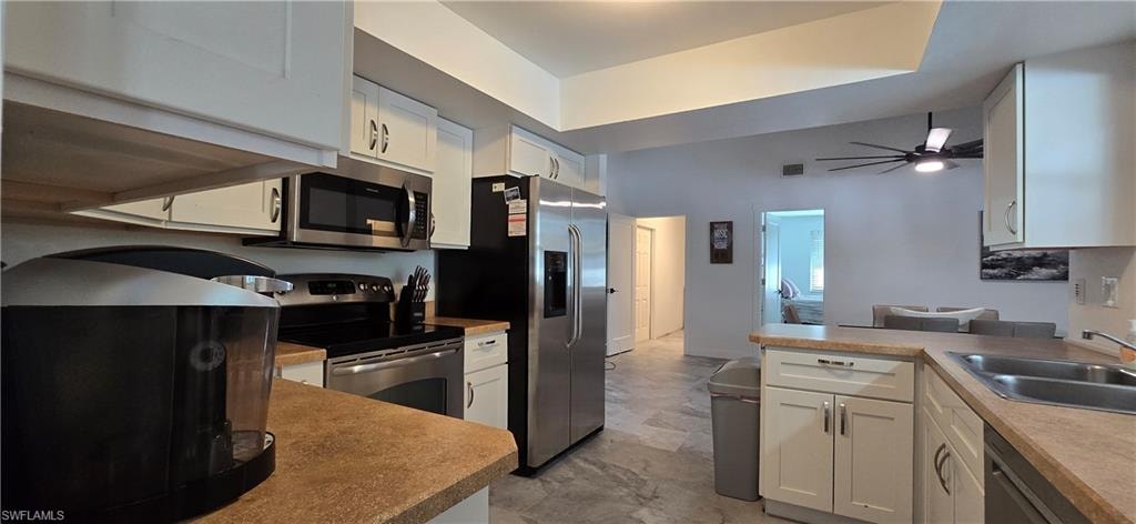 Kitchen featuring appliances with stainless steel finishes, a sink, a peninsula, white cabinetry, and ceiling fan
