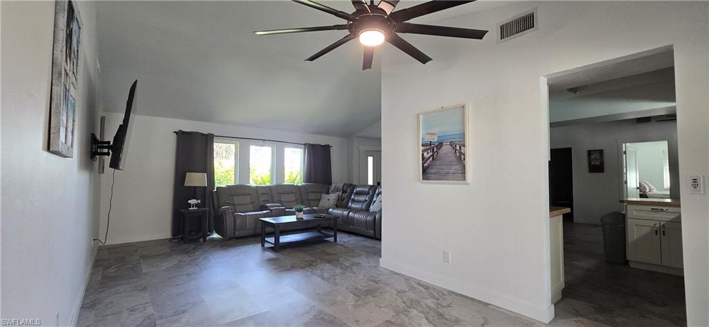 Living room featuring a ceiling fan, baseboards, and lofted ceiling