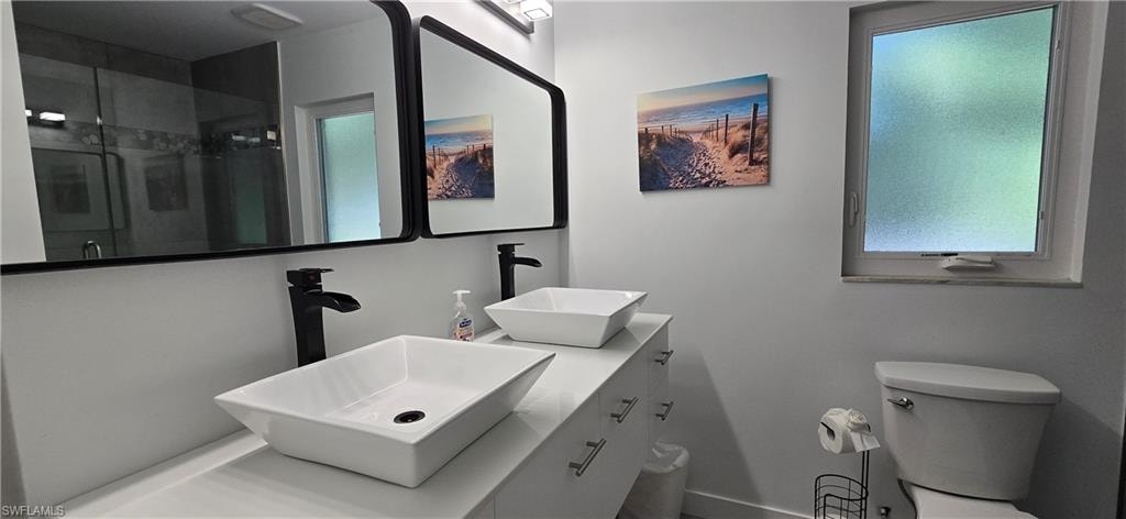 Full bath featuring a stall shower, baseboards, toilet, and double vanity