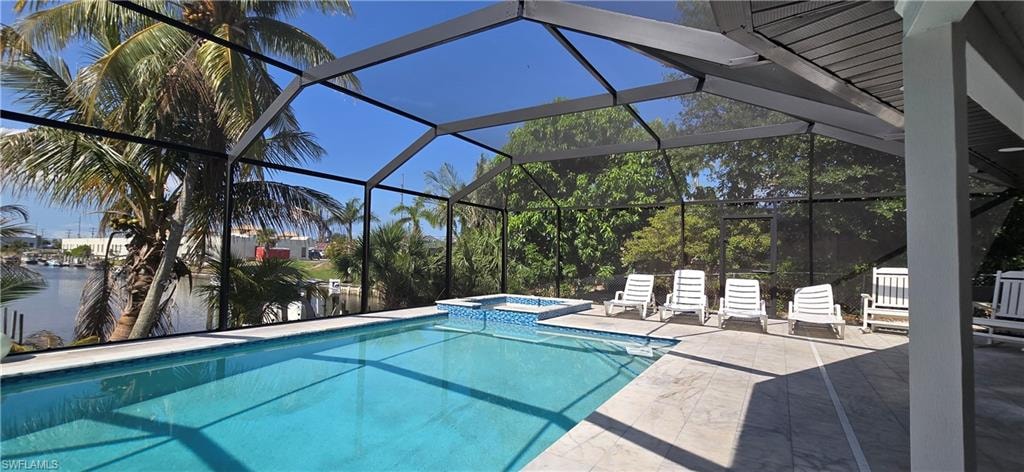 View of pool featuring a patio area, a pool with connected hot tub, a water view, and a lanai