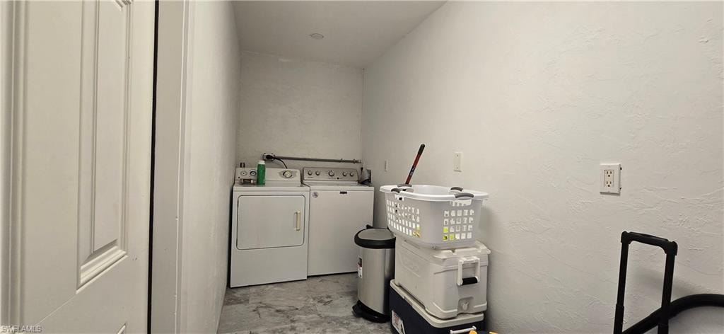 Clothes washing area featuring washing machine and clothes dryer and a textured wall