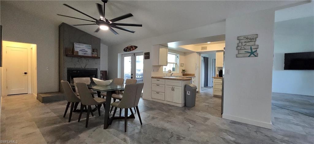 Dining area featuring a stone fireplace, a ceiling fan, and high vaulted ceiling