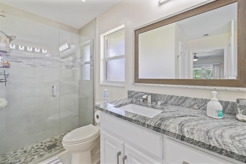 Full bath with a stall shower, toilet, vanity, and ceiling fan