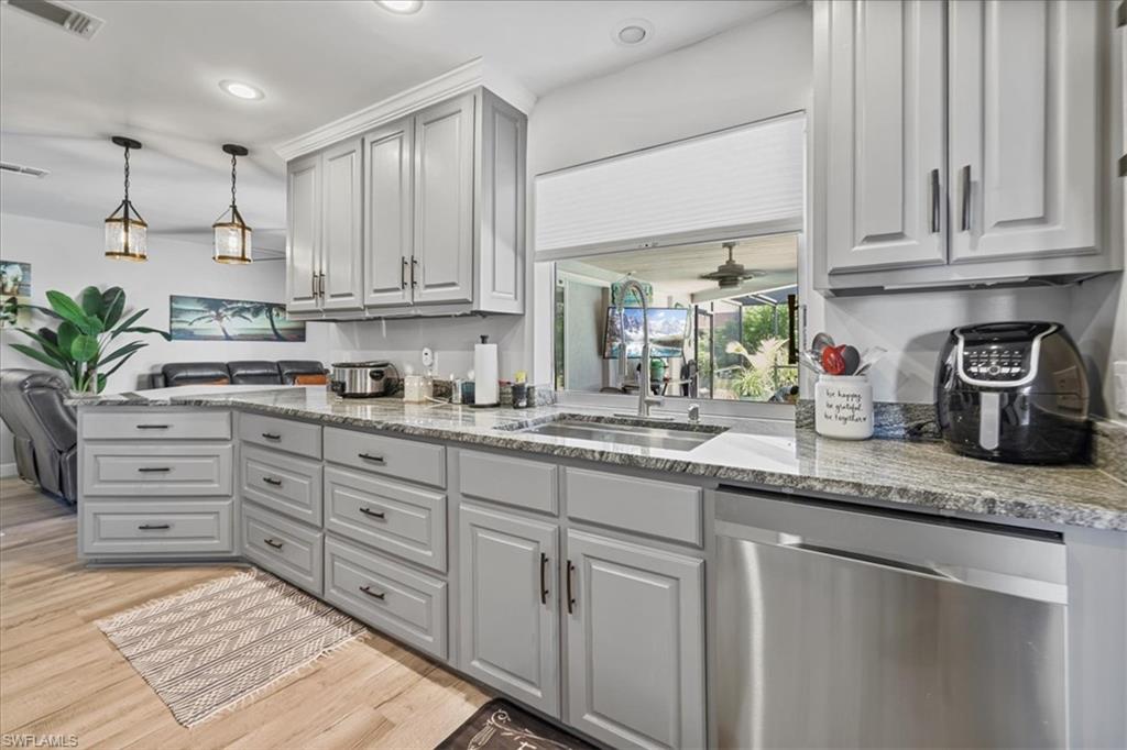 Kitchen with dishwasher, a sink, light wood-style flooring, light stone counters, and gray cabinetry
