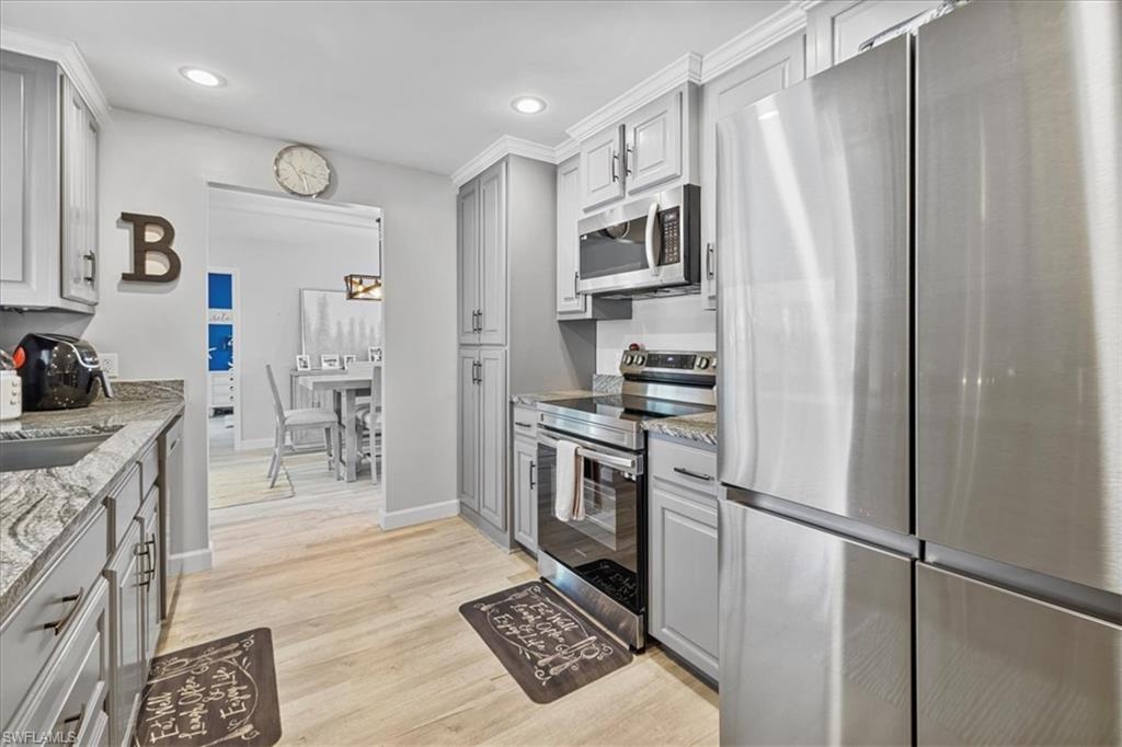 Kitchen featuring appliances with stainless steel finishes, gray cabinets, baseboards, light stone countertops, and light wood-type flooring