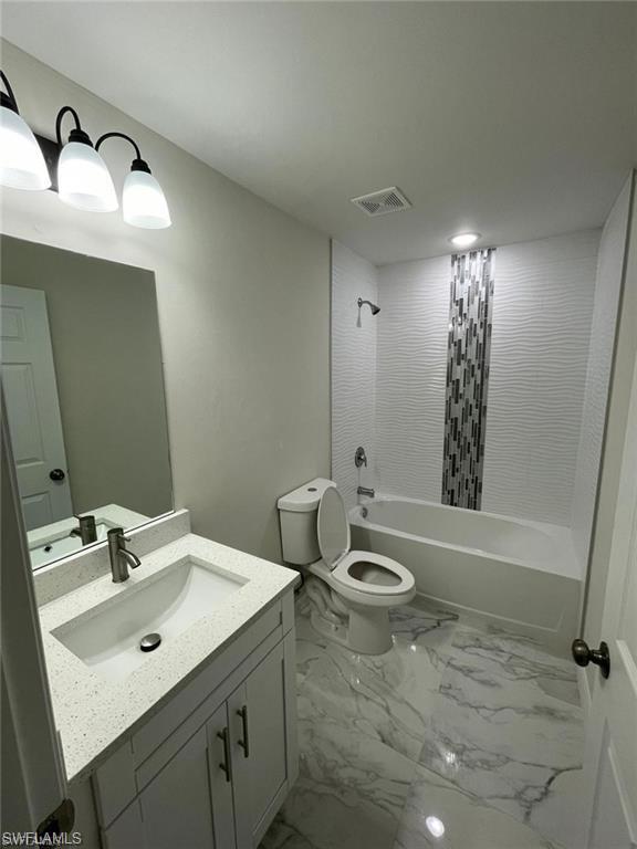 Bathroom with marble look tiles, vanity, toilet, and shower / bathtub combination