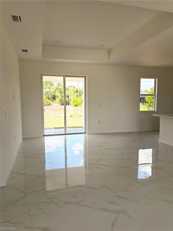 Empty room featuring a raised ceiling, baseboards, and light marble finish floors