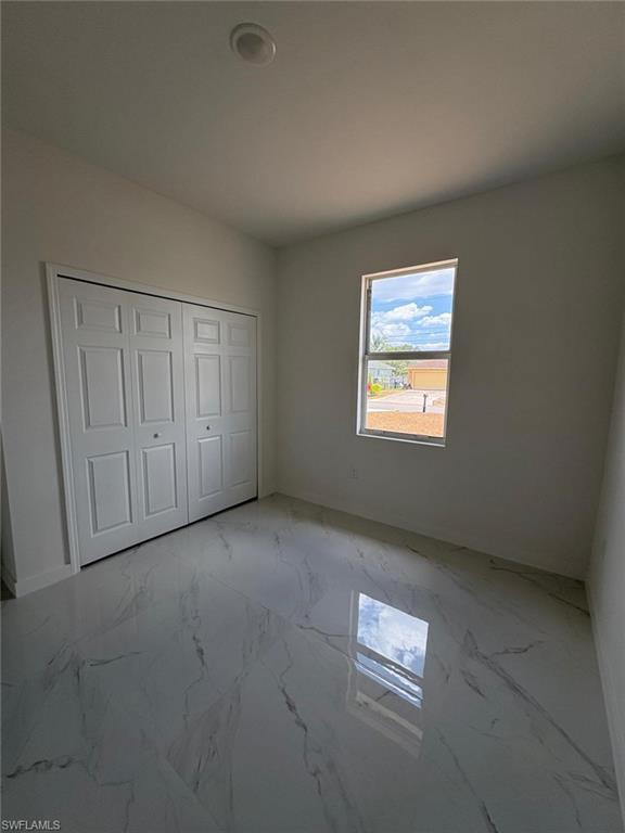 Unfurnished bedroom featuring light marble finish flooring, a closet, and baseboards