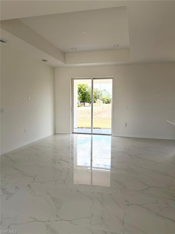Unfurnished room featuring a tray ceiling, baseboards, and light marble finish flooring