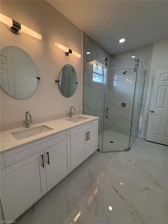 Full bath featuring marble look tile flooring, a marble finish shower, double vanity, and recessed lighting