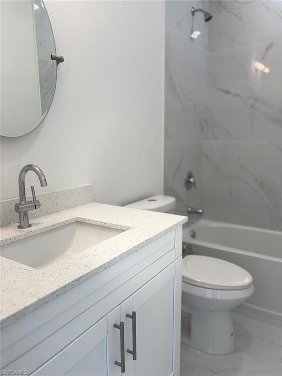 Full bath with vanity, toilet, marble look tiles, and shower / tub combination