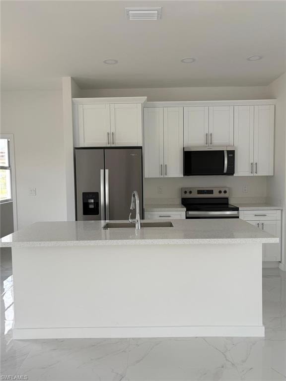 Kitchen with appliances with stainless steel finishes, light marble finish floors, an island with sink, white cabinets, and a sink