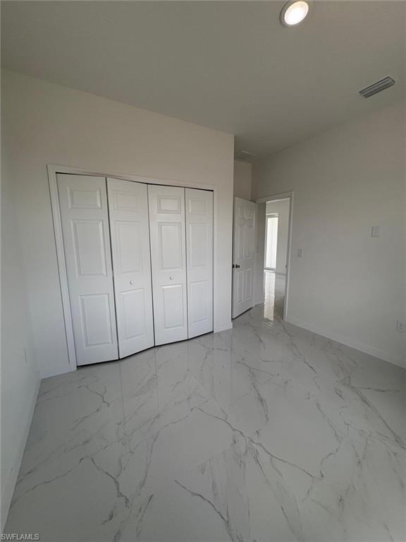 Unfurnished bedroom with baseboards, a closet, and marble finish flooring