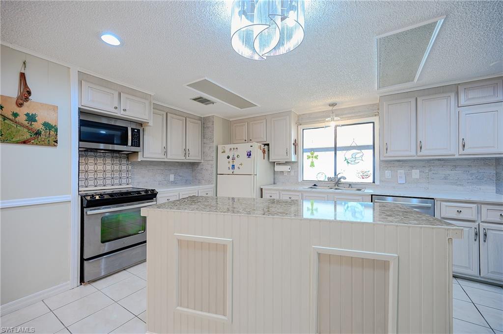 Kitchen with appliances with stainless steel finishes, a sink, light tile patterned floors, a textured ceiling, and a kitchen island
