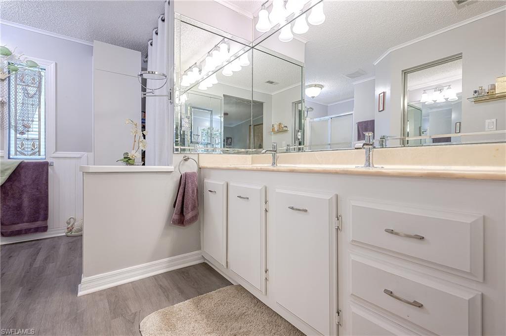Full bathroom with a textured ceiling, wood finished floors, vanity, crown molding, and a shower with door