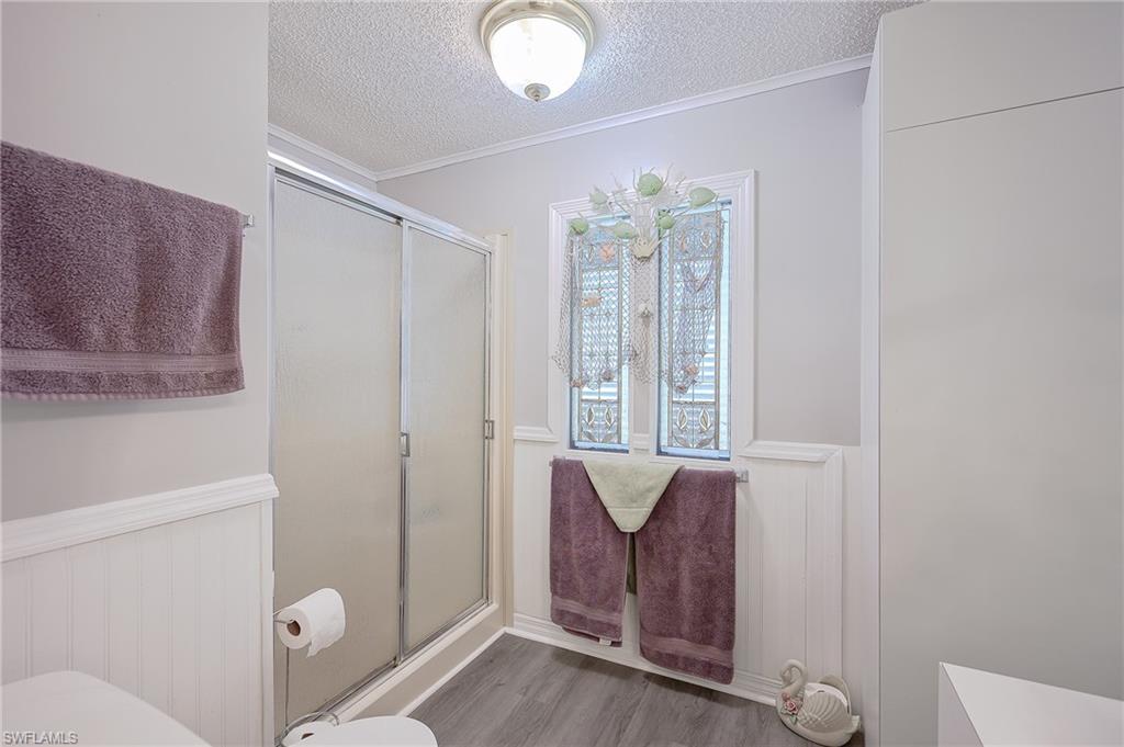 Bathroom featuring a textured ceiling, a stall shower, wood finished floors, wainscoting, and crown molding