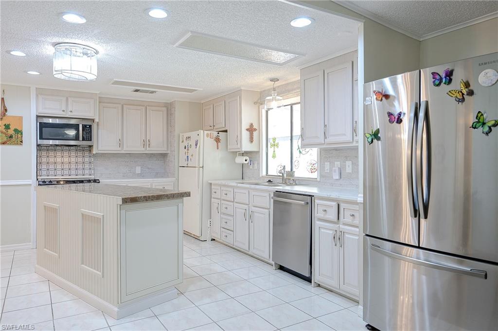 Kitchen with stainless steel appliances, a textured ceiling, decorative backsplash, a sink, and light countertops